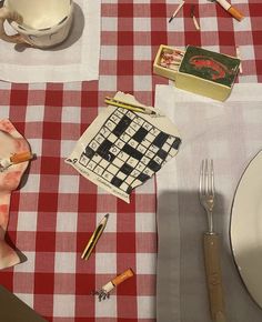 a red and white checkered table cloth with crosswords on it, silverware, utensils, and other items