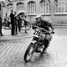 a man riding on the back of a motorcycle down a cobblestone street next to people