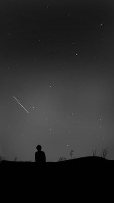 a man sitting on top of a hill under a sky filled with stars