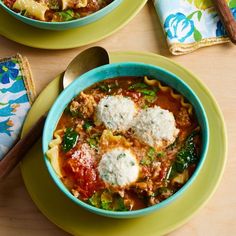 two bowls filled with pasta and sauce on top of a wooden table next to spoons