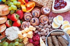 an assortment of food is displayed on a platter with fruit, bread and sausages