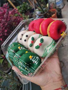 a hand holding a plastic container filled with frosted donuts and christmas decorations on them