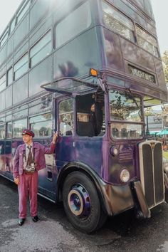 a man standing next to a purple double decker bus