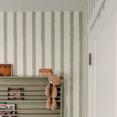 a teddy bear sitting on top of a book shelf in a room with striped walls