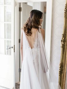 a woman standing in front of a mirror wearing a wedding dress with a long veil