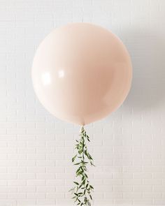 a balloon with some green leaves sticking out of it's side, against a white brick wall