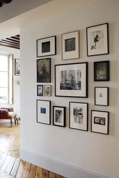 a white wall with many black and white framed pictures on it, along with wooden flooring