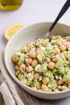 a white bowl filled with chickpeas and cucumber salad next to lemon wedges