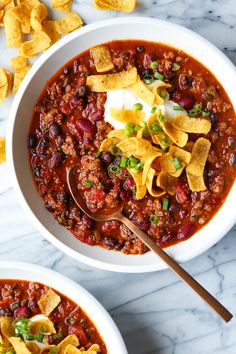 two bowls of chili with tortilla chips and sour cream on the side,