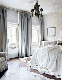 a white bed sitting in a bedroom next to a window covered in curtains and pillows