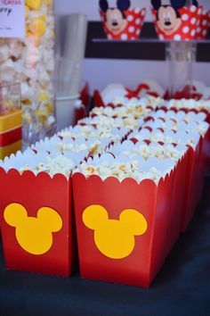 the table is set up with mickey mouse popcorn boxes and cups on it for guests to eat