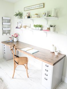 a desk and chair in a room with shelves on the wall above it, along with other items