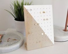 a white and gold card on a table next to a potted plant with two pairs of earrings