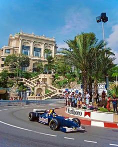 a man driving a racing car down a race track in front of a large building