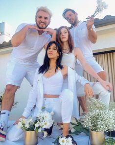 four people in white outfits posing for a photo with flowers on the ground behind them