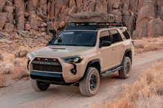 a tan four door suv driving down a dirt road