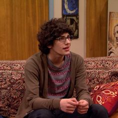 a young man sitting on top of a couch next to a red pillow in a living room