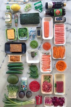 an array of food items laid out on a marble counter top, including carrots, broccoli, cucumbers and other vegetables