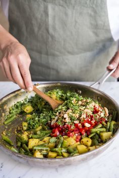 a person cooking vegetables in a pan with a wooden spoon