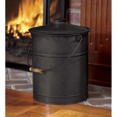 a black bucket sitting on top of a wooden floor in front of a fire place