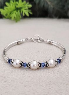 a bracelet with three pearls and blue beads on it, sitting next to a plant