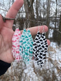 three small tasseled earrings hanging from a tree branch in the snow with trees in the background