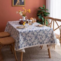 a dining room table covered with a blue and white flowered tablecloth next to two chairs