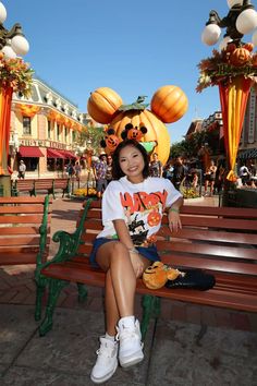 a woman sitting on top of a wooden bench in front of pumpkins and decorations