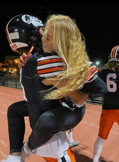 a football player is being hugged on the sidelines by another person with long blonde hair