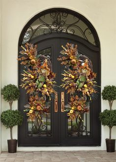 two wreaths on the front door of a house with potted plants and trees