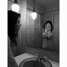 a woman standing in front of a bathroom mirror looking at her reflection and covering her face