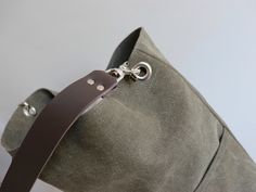 a gray bag with a brown leather strap hanging from it's side and a metal hook on the front