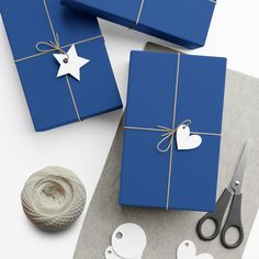 two blue wrapped gifts tied up with twine and paper heart tags next to scissors