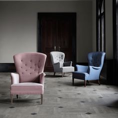 three different colored chairs in a room with wood flooring and black doors behind them