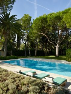 an empty swimming pool surrounded by trees and bushes with chaise lounges in the foreground