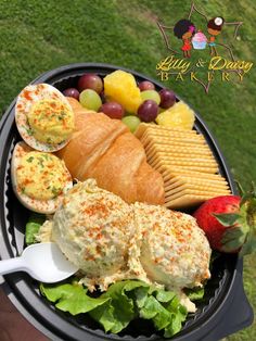 a plate with bread, cheese, fruit and crackers in it on the grass