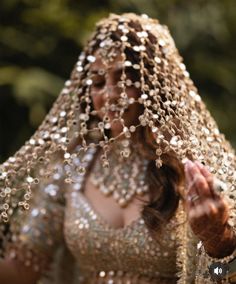 a woman in a gold and silver dress with beads on her head is holding out her hand