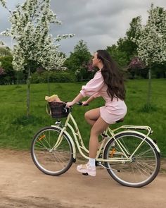 a woman riding a bike down a dirt road next to a lush green field with white flowers