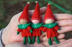 two small red and green christmas elves are held in the palm of someone's hand