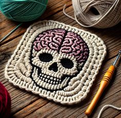 a crocheted square with a skull in the middle and yarn next to it