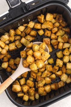 a pan filled with tater tots and a wooden spoon in the air fryer