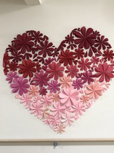 a heart made out of pink and red paper flowers on a white wall in the shape of a flower