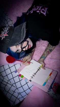 a woman with blue hair and glasses laying on a bed next to a notepad