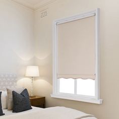 a white bed sitting under a window next to a night stand with two lamps on it