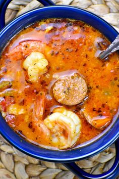 a blue bowl filled with soup and shrimp on top of a woven place mat next to a spoon