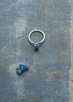 "A delicate ring in ombre sterling silver. The natural, raw, rough little blue sapphire is held by sturdy prongs. The band is reticulated slightly and hammered, giving the ring a unique, natural and personal feel. The silver is left raw, cleaned and unpolished. The prongs and the area around them have been gently dipped in patina, giving them a dark colour. This accentuates the bud-like look of the stone held in its prongs. Made to order in the size of your choice. The stones are around 6mm. The Raw Sapphire Ring, Raw Sapphire, Ring Blue Stone, Ring Blue Sapphire, Raw Stone Ring, Blue Sapphire Ring, Blue Stone Ring, Handmade Box, Tiny Earrings