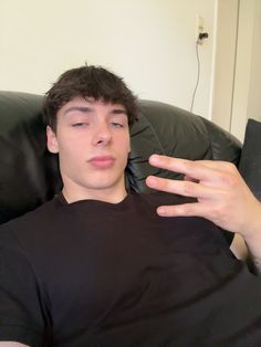 a young man sitting on top of a black couch holding his hand out to the side