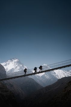 three people walking across a suspension bridge with mountains in the background