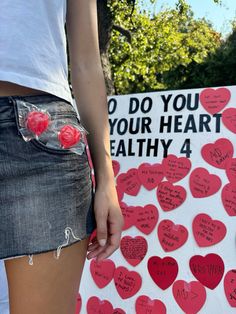 a woman standing in front of a sign that has hearts written on it and the words do you your heart healthy?