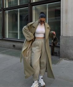 a woman walking down the street with her hand in her pocket and wearing white sneakers